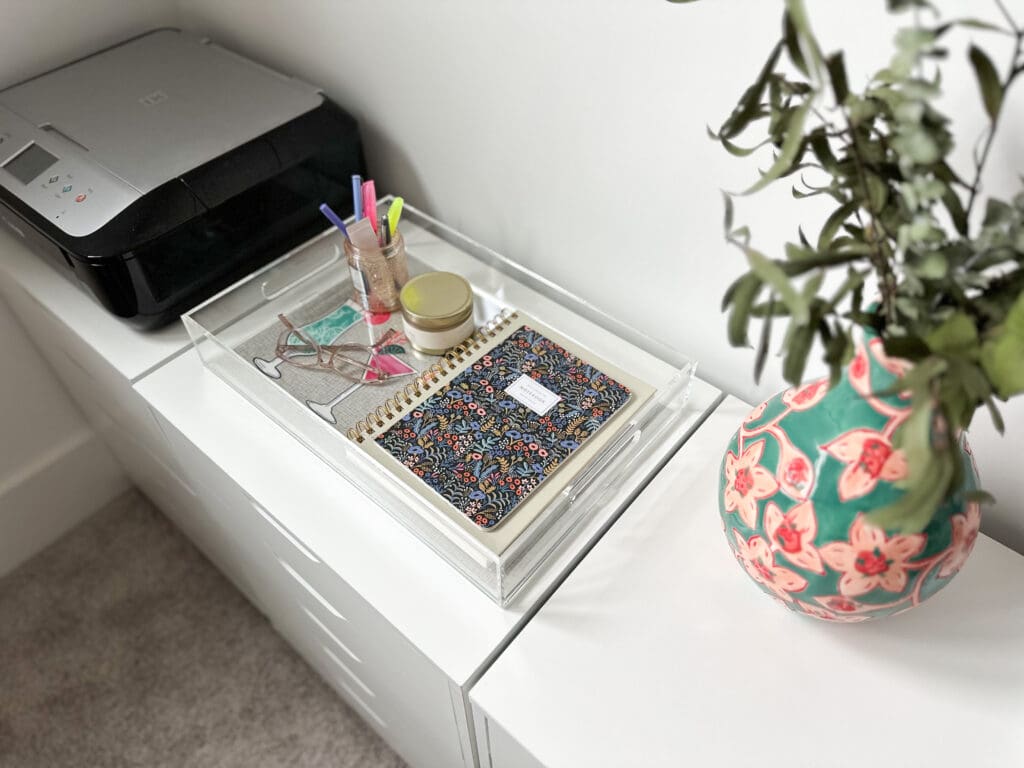 acrylic tray in a home office tidily holding supplies, sitting between a printer and turquoise vase