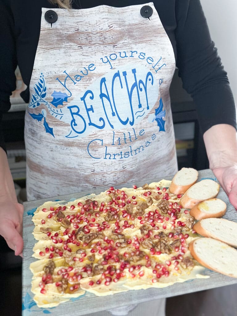 woman holding butter board wearing an apron that says "Have yourself a beachy little christmas"