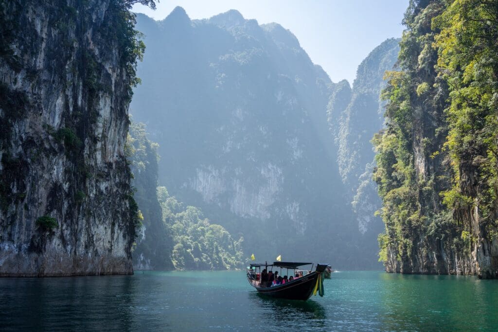 Traditional long boat in Phuket Thailand, floating serenely through rock formations covered in greenery