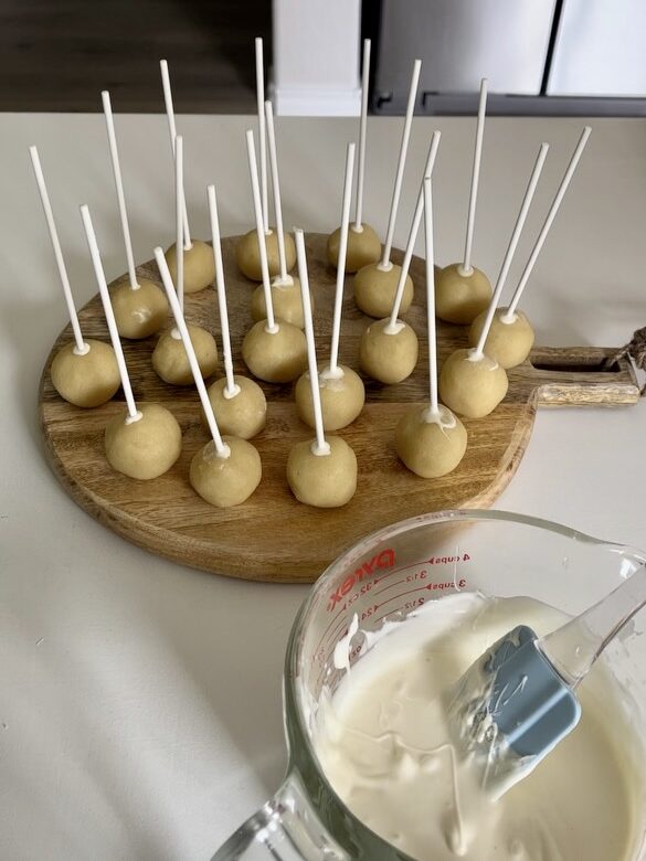 cake pops sitting on wood serving tray next to bowl of melted white chocolate