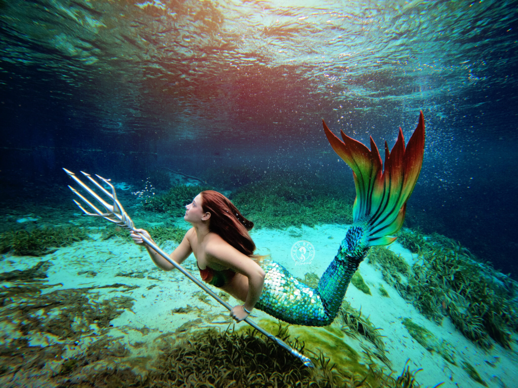 Woman in mermaid fin carrying trident under ocean