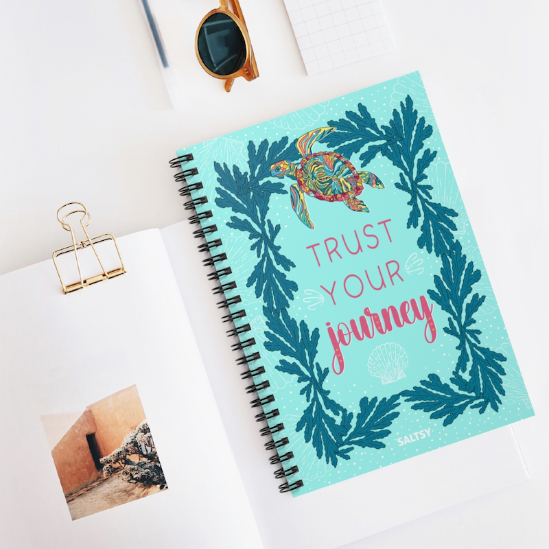 Creative affirmation sea turtle notebook that says "trust your journey". Beautiful journal cover shows a colorful sea turtle, blue sea plants, and white shells on a turquoise background.