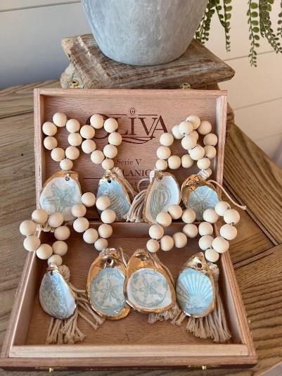 Elegant oyster shells with painted gold exteriors and blue and white ocean prints on the interior, tied to a ring of wooden beads and a tassel - intended for a napkin ring